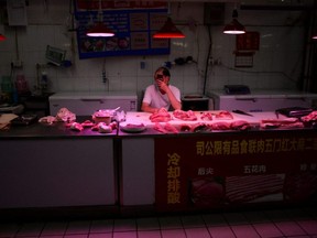 A pork vendor wearing a face mask uses his phone as he waits for customers at a meat stall inside a grocery market, following new cases of COVID-19 infections in Beijing, China, Monday, June 15, 2020.