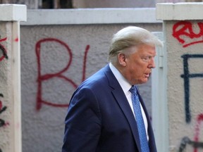 U.S. President Donald Trump walks past a building defaced with graffiti by protestors in Lafayette Park across from the White House on June 1, 2020.