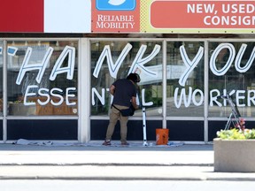 Joseph Pilapil puts the finishing touches on a Thank You Essential Workers window painting, on Portage Avenue on Tuesday.