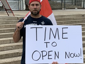Holding a Canadian flag and carrying a sign reading 'Time to Open Now,' Winnipegger Patrick Allard takes part in a small protest at the Manitoba Legislature in Winnipeg in early June.