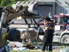 Two people embrace Friday while a front end loader is used to remove the campsites that were recently ordered vacated by the City of Winnipeg.