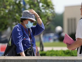 A woman wearing a mask holds onto her hat in the wind while waiting for a bus at Confusion Corner in Winnipeg on Mon., June 15, 2020.