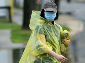 A woman wearing a rain poncho and a surgical mask walks near Central Park, in Winnipeg.