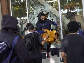 A person jumps from a store window during widespread protests and unrest in response to the death of George Floyd, on May 31, 2020 in Santa Monica, Calif.