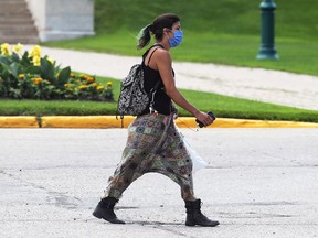 A woman wearing a mask walks in front of the Manitoba Legislative Building on Broadway in Winnipeg on Sunday.