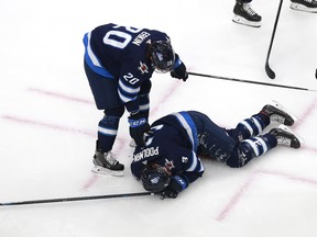 Winnipeg Jets' Cody Eakin checks on teammate Tucker Poolman as he lies on the ice after he was hit in the face with a puck during Tuesday's game against the Flames.