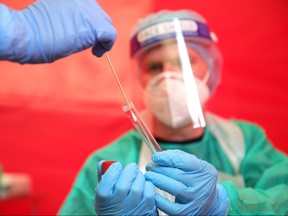 An employee of the Bonn professional firefighters places a throat swab sample into a tube held by a colleague from a woman seeking a test for possible COVID-19 infection at a test station on Aug. 24, 2020 in Bonn, Germany.