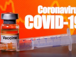 A small bottle labelled with a "Vaccine" sticker stands near a medical syringe in front of displayed "Coronavirus COVID-19" sign. 
Reuters file