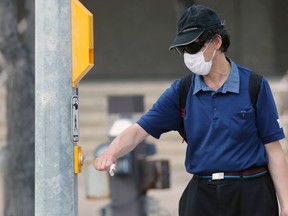 A man wearing a mask bumps the walk button on Portage Avenue at Dominion Street in Winnipeg on Wednesday.