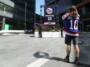 A man wearing a Dale Hawerchuk jersey takes a picture of his Winnipeg Jets Hall of Fame banner in True North Square in Winnipeg on Wednesday, Aug. 19, 2020.
