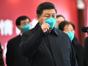 This photo released on March 10, 2020 by China's Xinhua News Agency shows Chinese President Xi Jinping wearing a mask as he gestures to a coronavirus patient and medical staff via a video link at the Huoshenshan hospital in Wuhan, China.