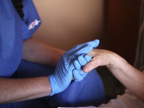A nurse wearing protective gloves holds the hand of a patient in a palliative care unit of a French hospital.