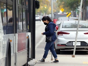 A woman wearing a mask boards a bus on Sherbrook Street in Winnipeg on Monday.