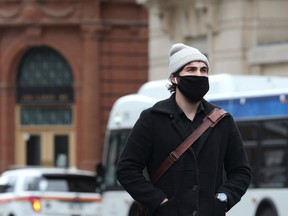 A bundled-up man wearing a mask crosses Portage Avenue at Garry Street in Winnipeg on Monday.