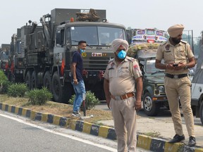 Punjab Police personnel stand guard near the Army convoy along a national highway blocked by farmers during a nationwide farmers' strike following the recent passing of agriculture bills in the Lok Sabha (lower house), on the outskirts of Amritsar, India, Sept. 25, 2020.