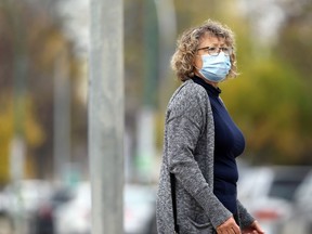 A woman wearing a mask waits to cross Broadway in Winnipeg on Monday.
