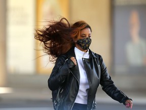 The hair of a woman wearing a mask blows in the wind as she crosses Portage Avenue at Vaughan Street in Winnipeg on Tuesday.