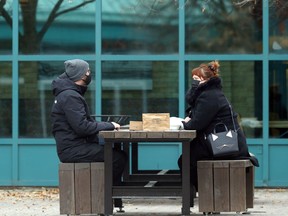 People wear masks and sit across a table outdoors at The Forks in Winnipeg on Sunday, Oct. 18, 2020.
