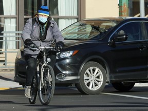 A man wearing a face mask cycles across Portage Avenue at Colony Street in Winnipeg on Monday.