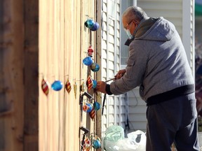 A man wears a face mask as he mounts Christmas decorations on a fence on Playgreen Crescent in Winnipeg on Tues., Nov. 3, 2020. Kevin King/Winnipeg Sun/Postmedia Network