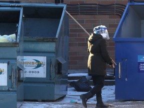 A person wearing Personal Protective Equipment uses a stick to open garbage can lids at the Maples Personal Care Home on Saturday.