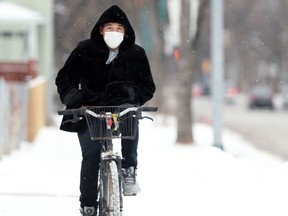 A man wearing a face mask keeps his hands warm in his pockets as he rides a bike along Redwood Avenue in Winnipeg on Sunday.