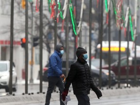 Two people cross Portage Avenue, in Winnipeg, while wearing masks on Tuesday.