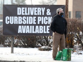 A person wears a mask while standing near a sign offering delivery and curbside pickup, in Winnipeg, during the Covid-19 pandemic..  Wednesday, November, 25/2020.Winnipeg Sun/Chris Procaylo/stf