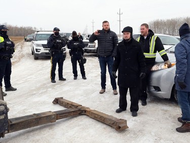 Minister Tobias Tissen (third from right) and another representative of Church of God, south of Steinbach, Man., stand between a tow truck hired by RCMP and a van it is preparing to tow off the highway on Sunday, Nov. 29, 2020.