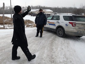 A representative of Church of God holds his phone up as an RCMP officer stands by a vehicle blocking the entrance to the property south of Steinbach, Man., on Sunday, Nov. 29, 2020.