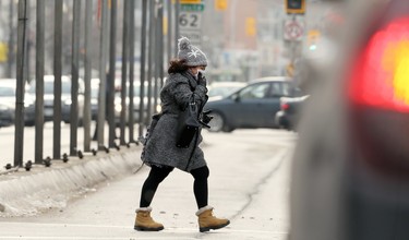A woman holds onto her face mask as she crosses Portage Avenue in a strong wind in Winnipeg on Wed., Nov. 25, 2020. Kevin King/Winnipeg Sun/Postmedia Network