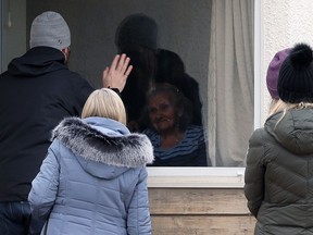 A group of people visit a resident at Charleswood Care Centre on Roblin Boulevard in Winnipeg through a window on Tuesday. Public health officials announced 10 more deaths linked to outbreaks at long-term care facilities in Manitoba including four deaths connected to the outbreak at Charleswood Care Centre.