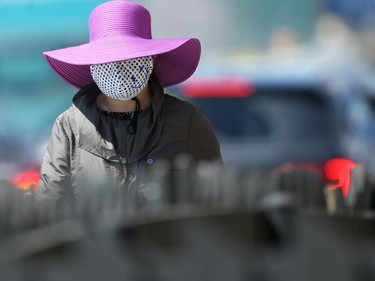 A woman walks along a street in Winnipeg while wearing a large hat and a mask.  Wednesday, May 27, 2020.