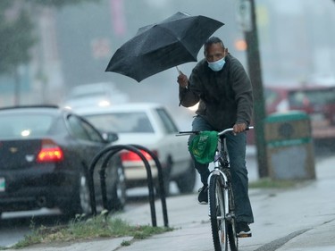 A man wears a mask and uses an umbrella while riding a bicycle along Main Street, in Winnipeg.   Thursday, Aug. 13, 2020.