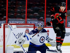 Senators left winger Brady Tkachuk (right) tips a shot on Jets goaltender Connor Hellebuyck last night. ERROL MCGIHON/Postmedia