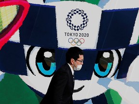 A man wearing a protective mask walks past a large poster featuring Tokyo 2020 Olympic Games mascot Miraitowa in Tokyo, June 4, 2020.