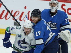 Winnipeg Jets centre Adam Lowry (centre) ties up Vancouver Canucks forward Tanner Pearson in front of goaltender Connor Hellebuyck in Winnipeg on Tuesday, Jan. 14, 2020.