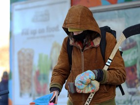 A man wearing a mask cradles a hockey stick as he prepares to enter a store on Maryland Street in Winnipeg on Mon., Jan. 4, 2021. Kevin King/Winnipeg Sun/Postmedia Network
