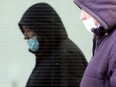 A person is reflected in glass while wearing a mask and walking through downtown Winnipeg on Saturday, Jan. 9, 2021.