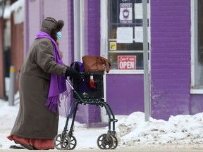 A person wearing a mask and a heavy jacket walks past a shop with an open sign in the window, in Winnipeg on Friday, Jan. 22, 2021 in Winnipeg.