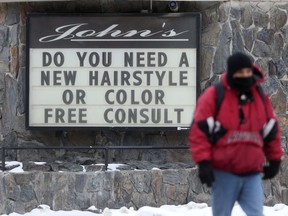 A person walks past a sign regarding salon services, in Winnipeg. Limited changes to the public health orders took effect Saturday which are set to last for three weeks.