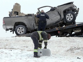 A police officer looks at a vehicle involved in what RCMP describe as a fatal, single-vehicle collision on the west Perimeter Highway between Portage Avenue and Roblin Boulevard in Winnipeg while a tow truck employee collects debris on Monday, Jan. 25, 2021. RCMP say a 28-year-old man is dead after crashing into a pole while driving in slippery conditions.