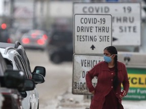 A person walks near signs for a COVID-19 testing site, in Winnipeg on Saturday.