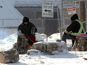 Two men sit around a fire near a COVID-19 testing site at Thunderbird House in Winnipeg on Sunday, Jan. 31, 2021.