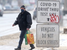 A person walks past signs for a COVID-19 test site on Main Street, in Winnipeg on Tuesday, Feb. 2, 2021.