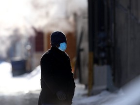 A person wears a mask while passing an alley that is full of frozen exhaust gas from a building, in downtown Winnipeg on Saturday, Feb. 6, 2021.