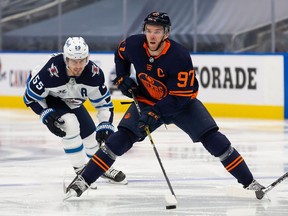 EDMONTON, AB - FEBRUARY 17: Connor McDavid #97 of the Edmonton Oilers skates the puck against Mark Scheifele #55 of the Winnipeg Jets at Rogers Place on February 17, 2021 in Edmonton, Canada.