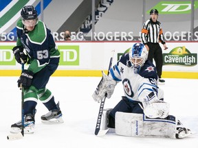Goalie Laurent Brossoit of the Winnipeg Jets makes a glove save with Bo Horvat (53) of the Vancouver Canucks standing in front during NHL hockey action at Rogers Arena on Friday, Feb. 19, 2021 in Vancouver.