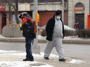 Two men wearing masks cross paths in downtown Winnipeg on Monday, Feb. 1, 2021.