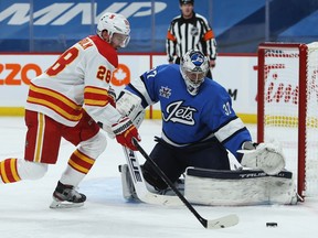 Winnipeg Jets goaltender Connor Hellebuyck tracks a rebound with Calgary Flames centre Elias Lindholm on the doorstep in Winnipeg on Mon., Feb. 1, 2021. Kevin King/Winnipeg Sun/Postmedia Network